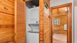 Un intérieur en bois avec un lave-linge et un sèche-linge intégrés, une petite fenêtre et une porte donnant sur une autre pièce.