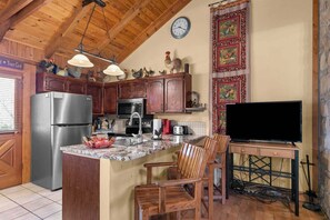 Een keuken met houten kastjes, een roestvrijstalen koelkast, een magnetron, een spoelbak en een televisie op een standaard.