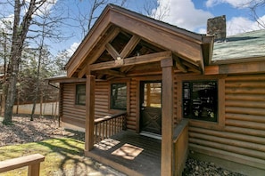 A log cabin with a porch, a chimney, and a window with a view.