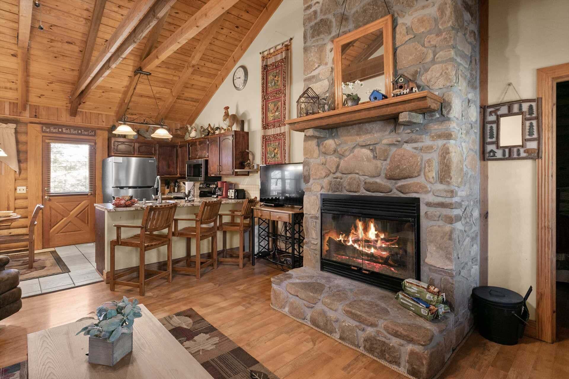 Un intérieur rustique avec une cheminée en pierre, des poutres apparentes en bois au plafond et un coin cuisine.