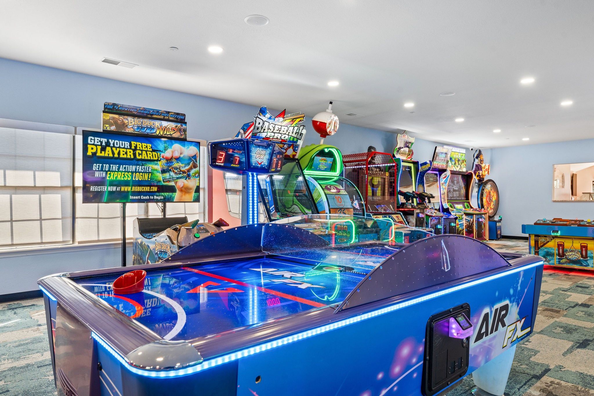 A room with arcade games, including a large air hockey table and various other gaming machines.