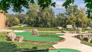 A miniature golf course with green artificial turf, stone obstacles, and a concrete path. - Private Cabin with Whirlpool Tubs, Free Wifi, 150 Beautiful Acres (Branson)