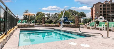 A swimming pool with a lifeguard stand, lounge chairs, and a stone wall.
