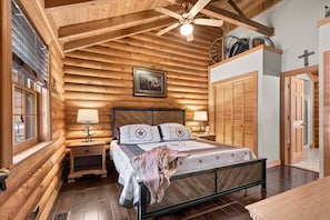 Ein schlafzimmer im Stil eines Blockhauses mit einem Bett, zwei Nachttischen, einem Deckenventilator und einem gerahmten Bild an der Wand.