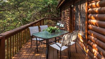 Una terraza de madera con una mesa y sillas de vidrio, rodeada de árboles.