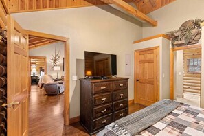 A log cabin interior with a wooden dresser, a television, and a bed with a quilt.