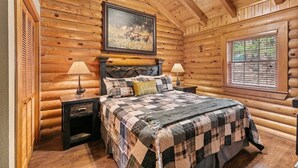 Un dormitori de cabana de fusta amb un llit, dues tauletes de nit, un capçal de llit, un quadre, una finestra i una làmpada.