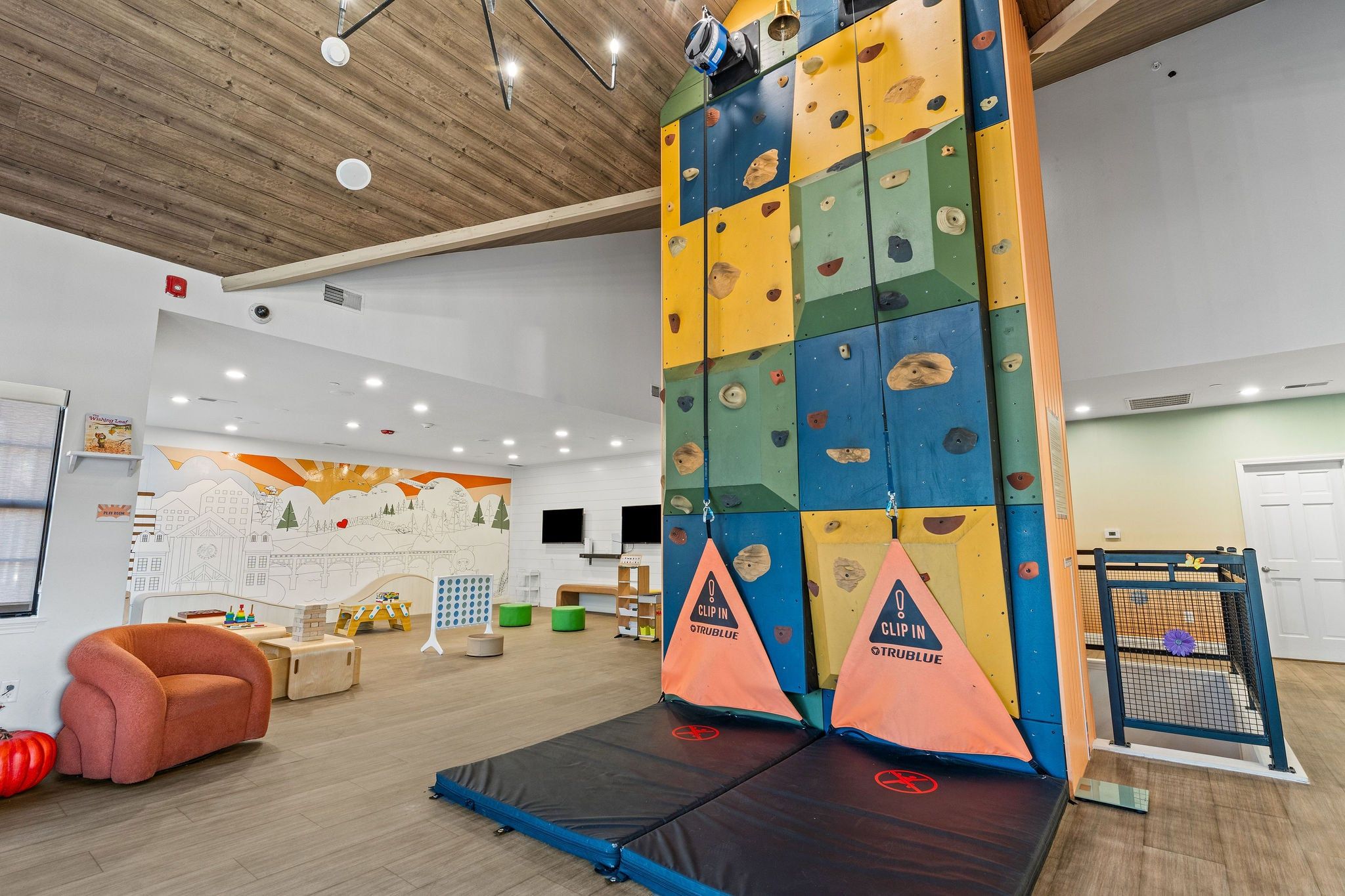 An indoor climbing area with a padded landing area, climbing walls, and a mural on the wall.