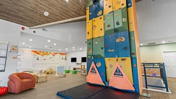 An indoor climbing area with a padded landing area, climbing walls, and a mural on the wall.