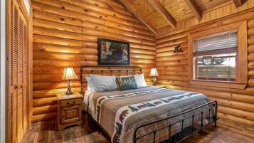 A log cabin bedroom with a bed, two bedside tables, a window, and a painting on the wall.