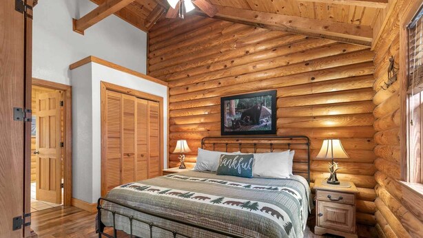 Une chambre dans un chalet en rondins, avec un lit, des lampes de chevet, un tableau encadré au mur et une porte en bois.