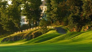 Un parcours de golf avec une clôture en bois, des collines verdoyantes et une construction visible au loin.