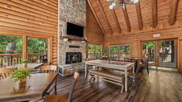 A log cabin interior with a stone fireplace, wooden dining table, and multiple seating arrangements.