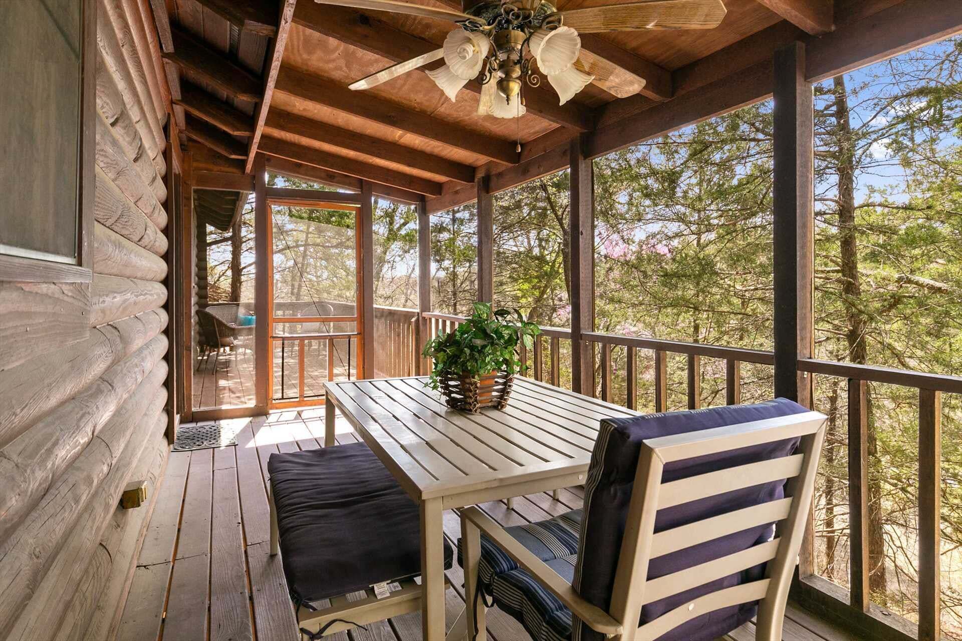 A wooden deck with a table and chairs, a ceiling fan, and a view of trees.