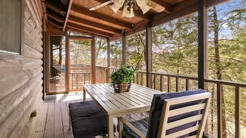 A wooden deck with a table and chairs, a ceiling fan, and a view of trees.