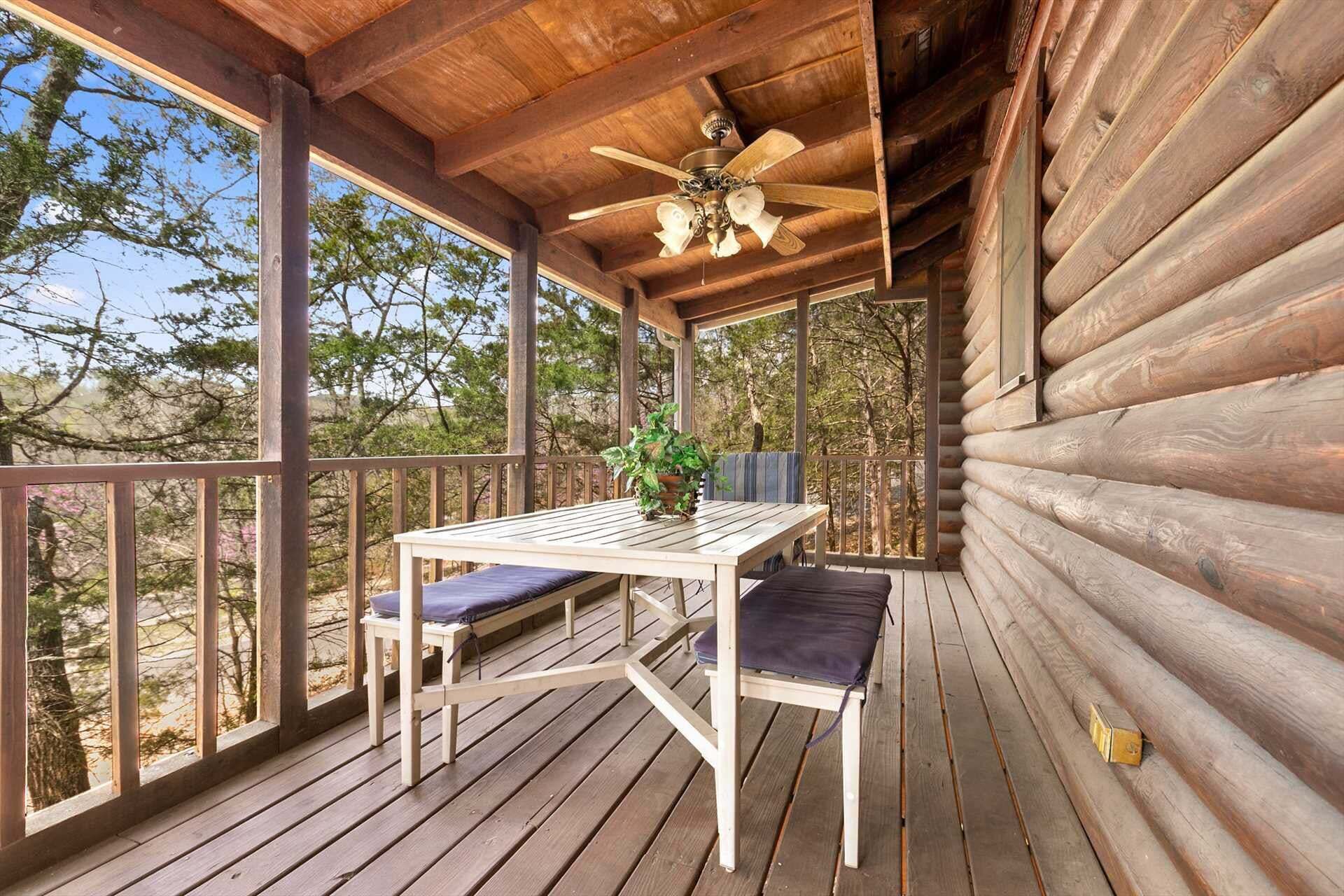 Une terrasse en bois avec une table et des chaises, un ventilateur de plafond et une vue sur les arbres.