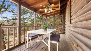 Une terrasse en bois avec une table et des chaises, un ventilateur de plafond et une vue sur les arbres.