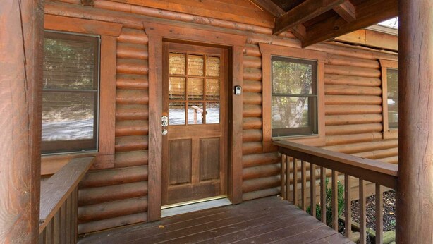 A log cabin with a wooden front door, windows, and a porch with a railing. - Log Cabin with Fireplace, Soaker Tubs, King Suites, Free Wifi (Branson)