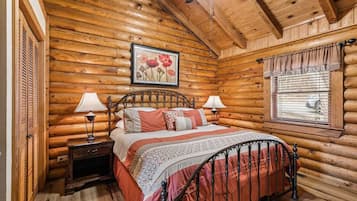 Une chambre à coucher située dans une cabane en rondins, avec un lit, deux tables de chevet, une fenêtre avec des stores et un ventilateur de plafond.