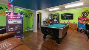 A pool table in a room with green walls, a poster advertising an event, and a television mounted on the wall. - Log Cabin with Fireplace, Soaker Tubs, King Suites, Free Wifi (Branson)