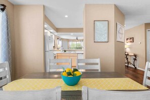 A dining area with a table set for two, a bowl of fruit, and a view into the kitchen. - Cozy Condo_ Free Daily Attraction Tickets_ Close to Branson (Branson)