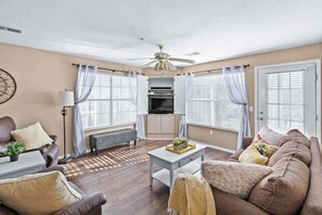 A living room with a sofa, a coffee table, a TV, and a ceiling fan. - Cozy Condo_ Free Daily Attraction Tickets_ Close to Branson (Branson)