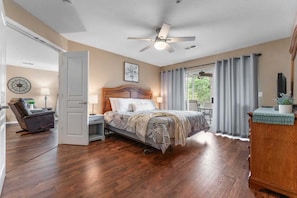 A bedroom with a bed, a ceiling fan, a nightstand, a chair, a window with curtains, and a view of greenery outside. - Cozy Condo_ Free Daily Attraction Tickets_ Close to Branson (Branson)