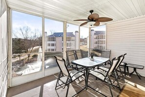 A sunroom with a table and chairs, large windows, a ceiling fan, and a view of residential buildings. - Cozy Condo_ Free Daily Attraction Tickets_ Close to Branson (Branson)