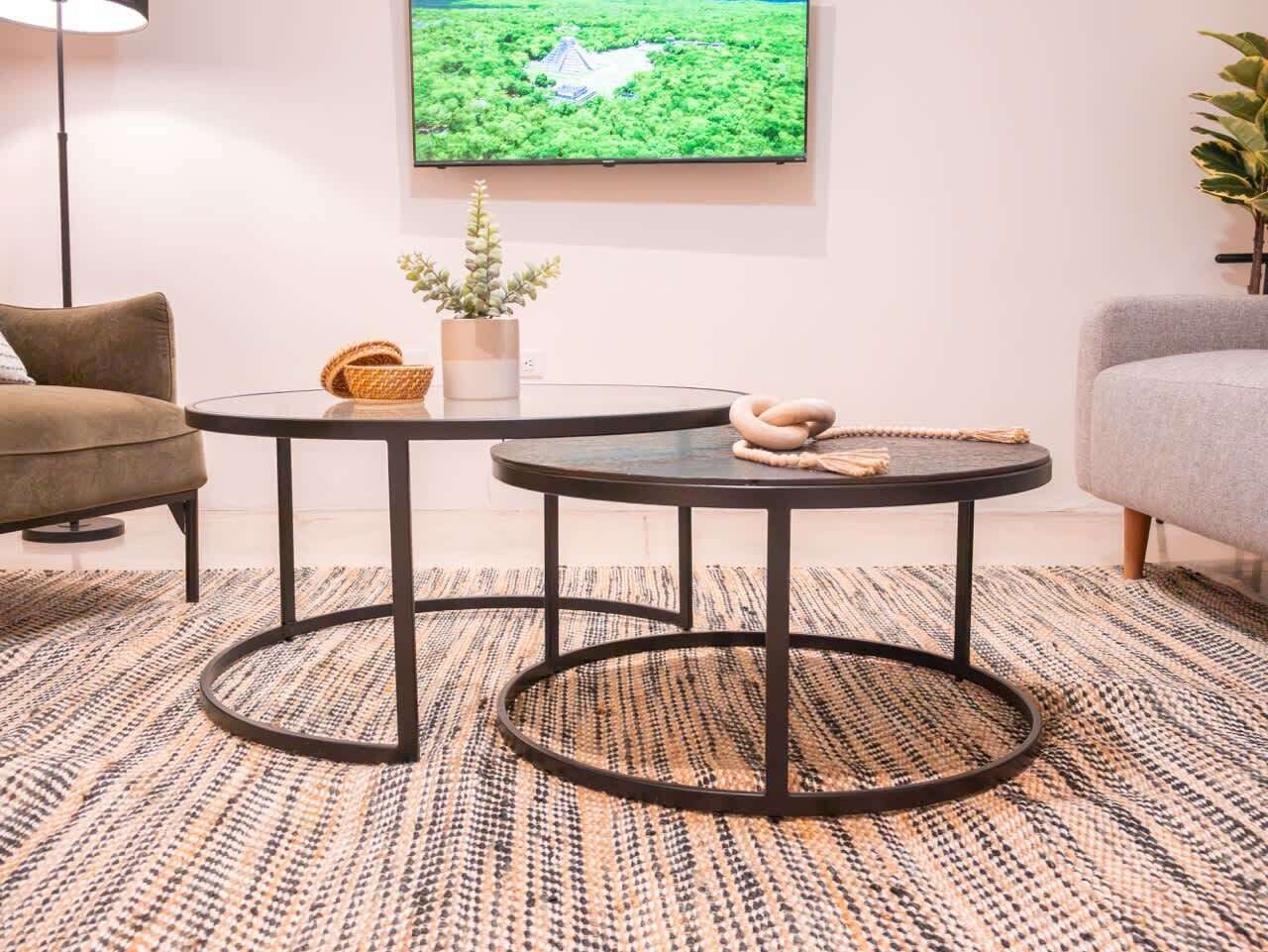 A room with two round tables, a sofa, a floor lamp, a television, and a patterned rug.