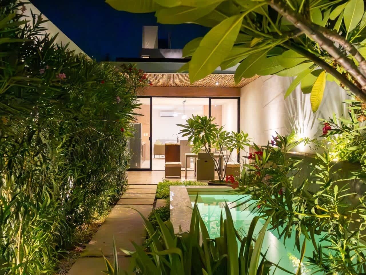 A modern house with a swimming pool, surrounded by lush greenery and a well-lit interior.