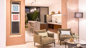 Un salón moderno con dos sillones, una mesa de centro de cristal y una cocina al fondo.