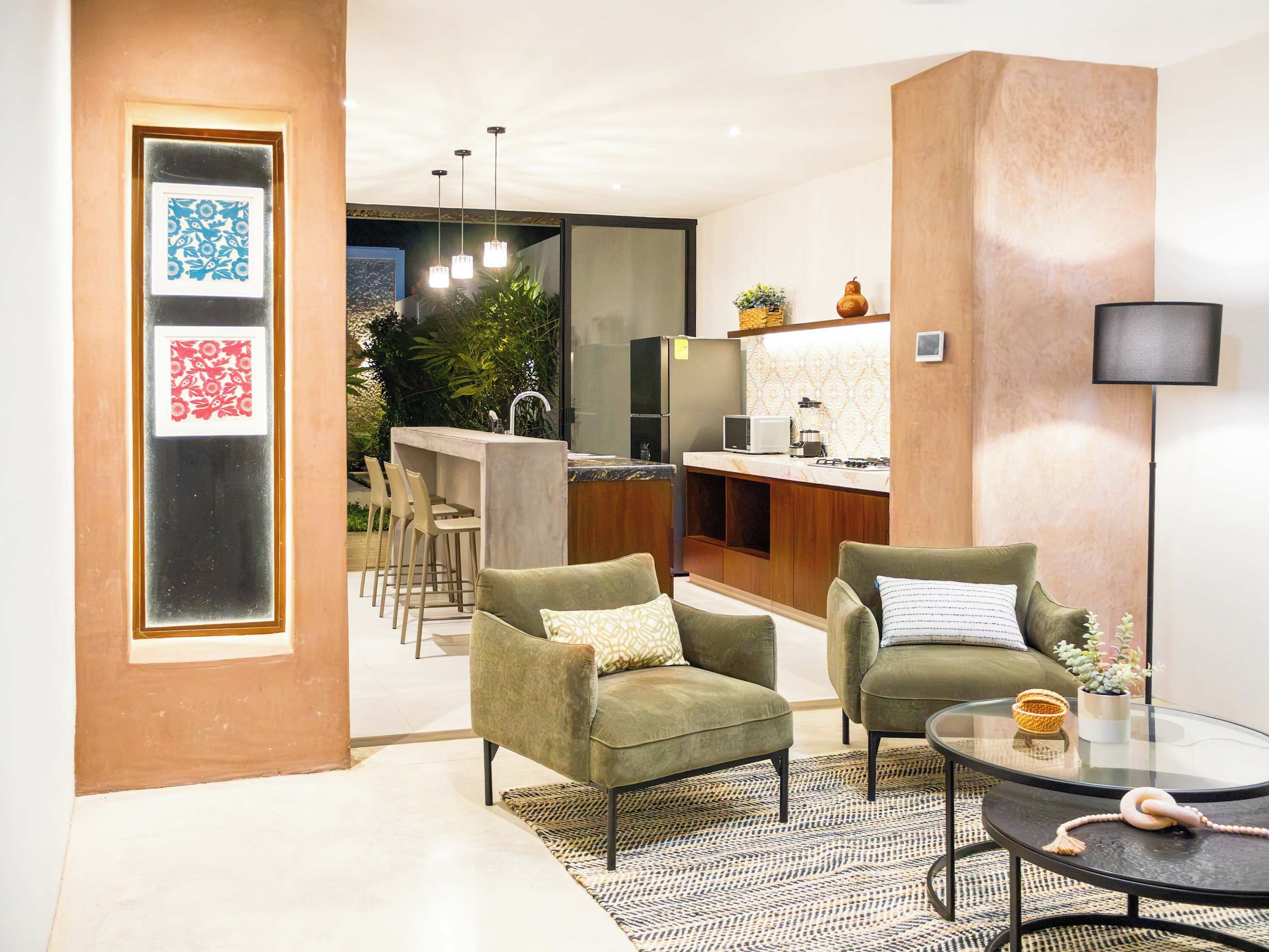 Uma sala de estar moderna com dois poltronas verdes, uma mesa de centro de vidro e uma área de cozinha com balcão.