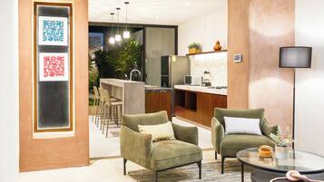 Una sala de estar moderna con dos sillones verdes, una mesa de centro de vidrio y una zona de cocina con barra.