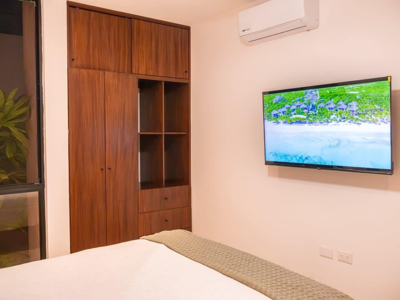 Un dormitorio con una cama, un armario de madera, un televisor montado en la pared y un equipo de aire acondicionado.