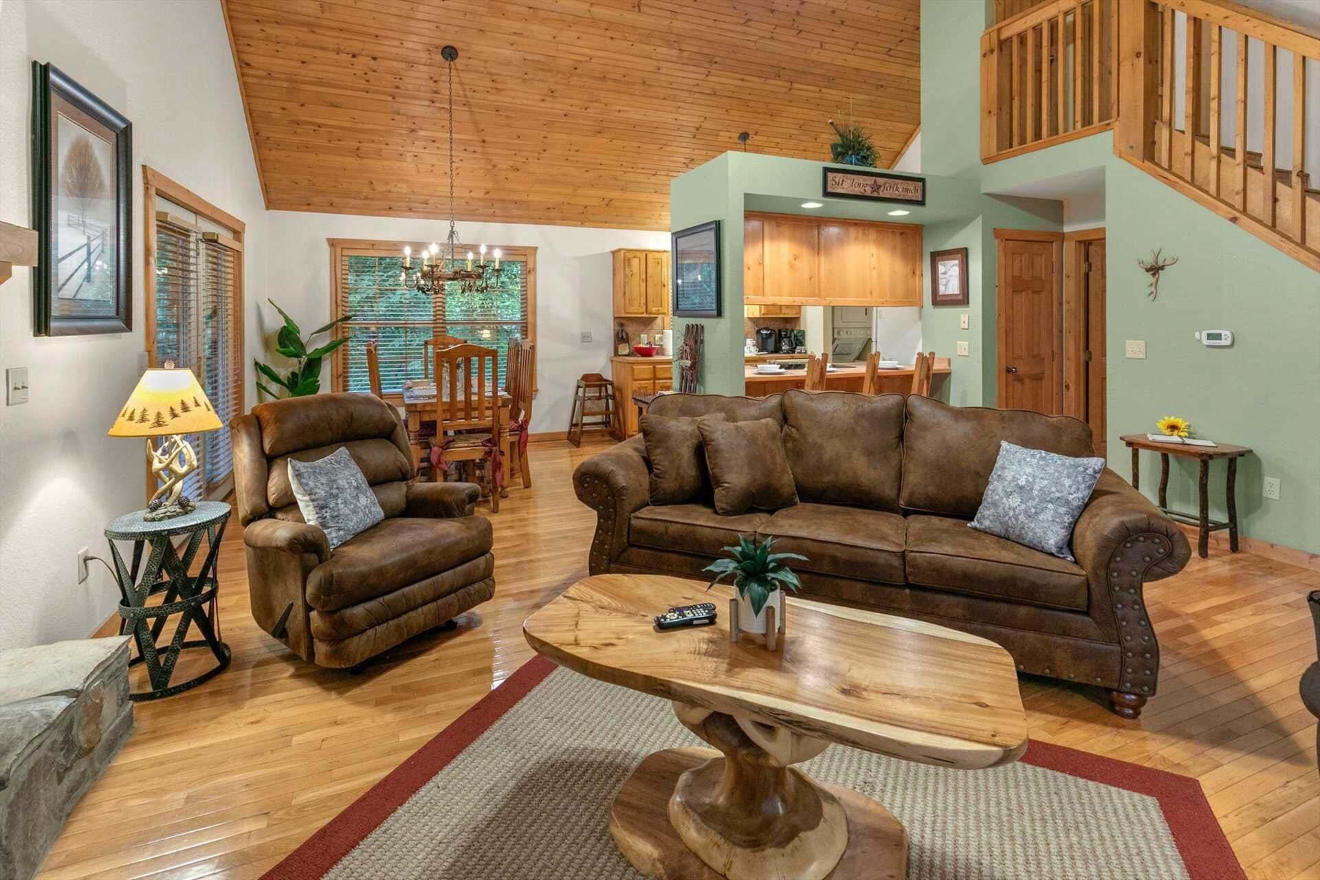 A spacious living room with a brown leather sofa, a wooden coffee table, and a dining area with wooden furniture.