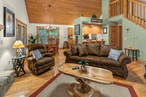 A spacious living room with a brown leather sofa, a wooden coffee table, and a dining area with wooden furniture.