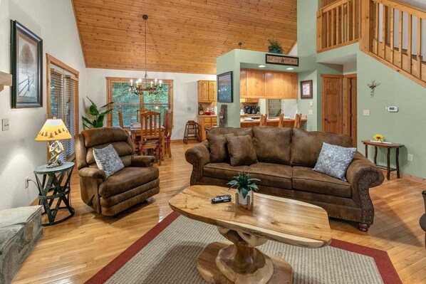 A spacious living room with a brown leather sofa, a wooden coffee table, and a dining area with wooden furniture.