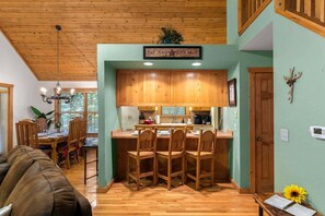 A dining area with wooden chairs and a table, a kitchen with wooden cabinets, and a sign above the counter.