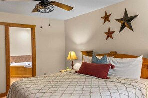 A bedroom with a bed, a wooden headboard, a nightstand with a lamp, and a door leading to another room.