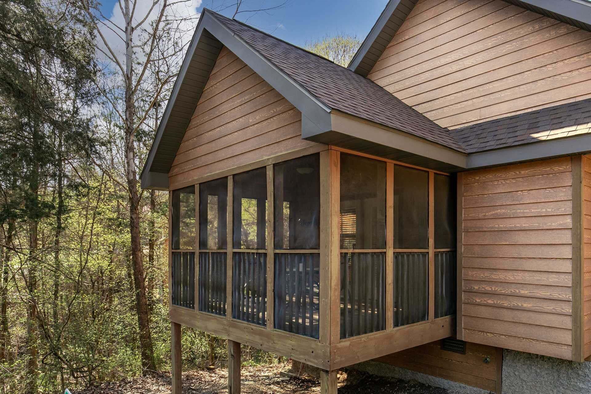 A wooden cabin with a large windowed porch, surrounded by trees.