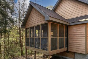 A wooden cabin with a large windowed porch, surrounded by trees.