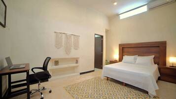 Habitación de hotel con cama, escritorio, silla y una alfombra estampada.