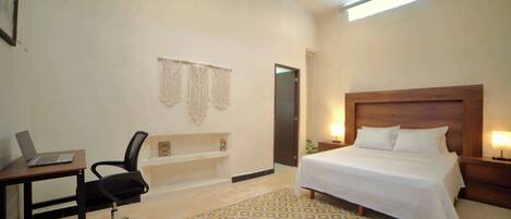 A hotel room with a bed, desk, chair, and a patterned rug.