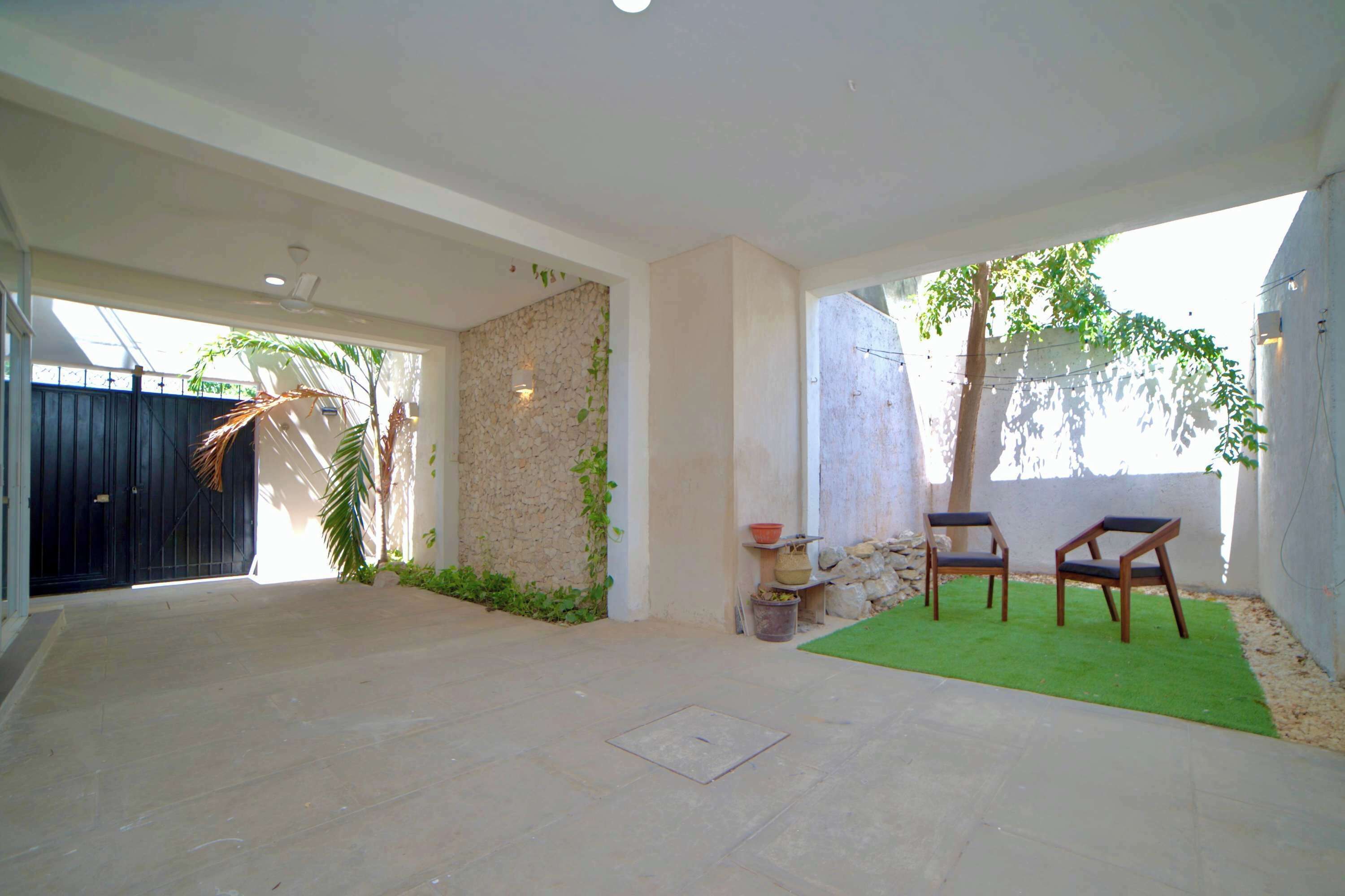 Un patio spacieux avec un mur en pierre, un petit jardin avec de la pelouse et deux chaises en bois.