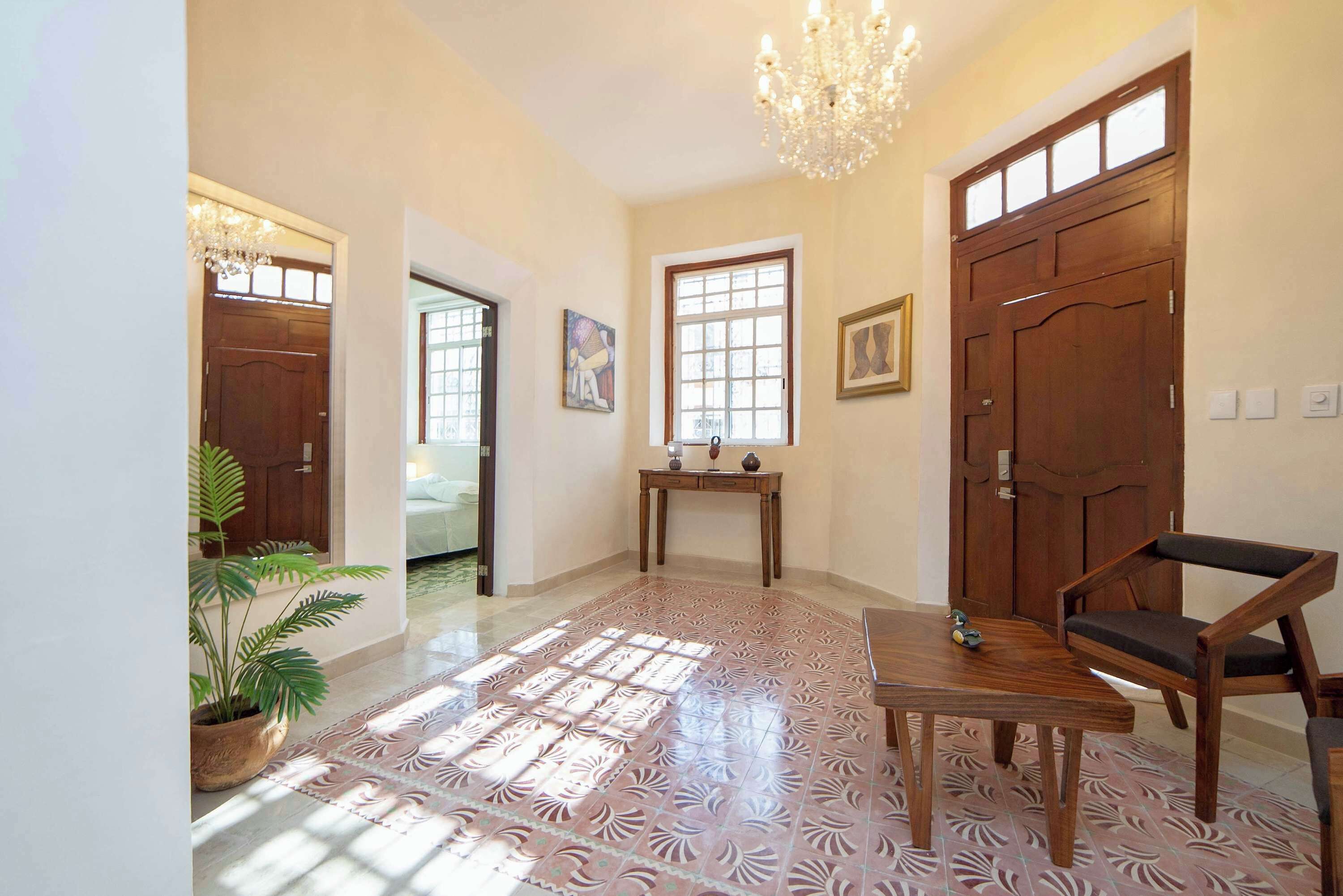 A spacious hallway with a chandelier, wooden doors, a table with chairs, and a patterned floor.