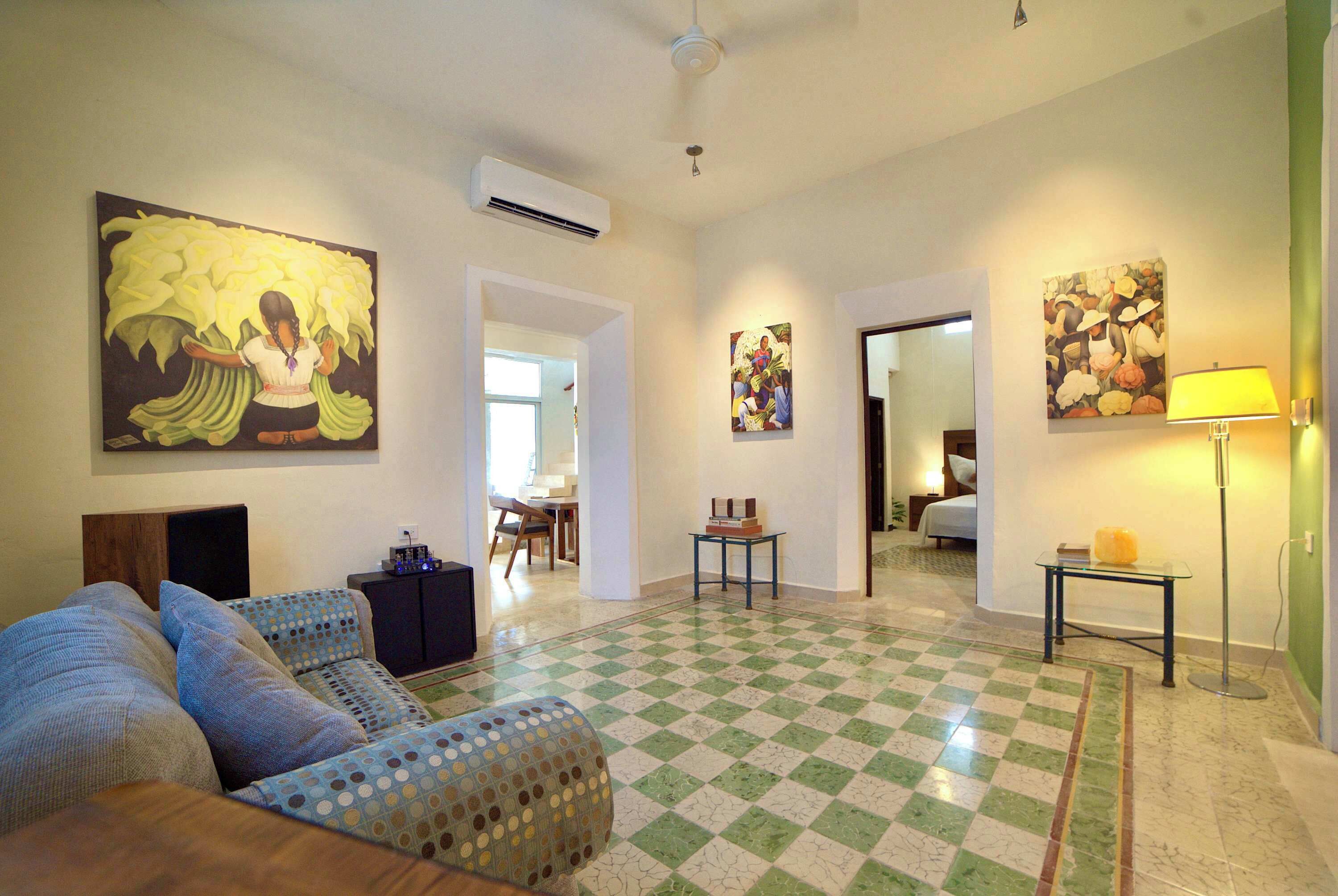 Une chambre d’hôtel avec un sol à carreaux, un canapé, un lit, une table et des œuvres d’art accrochées aux murs.