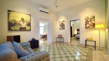 Habitación de hotel con piso de cuadros, un sofá, una cama, una mesa y obras de arte en las paredes.