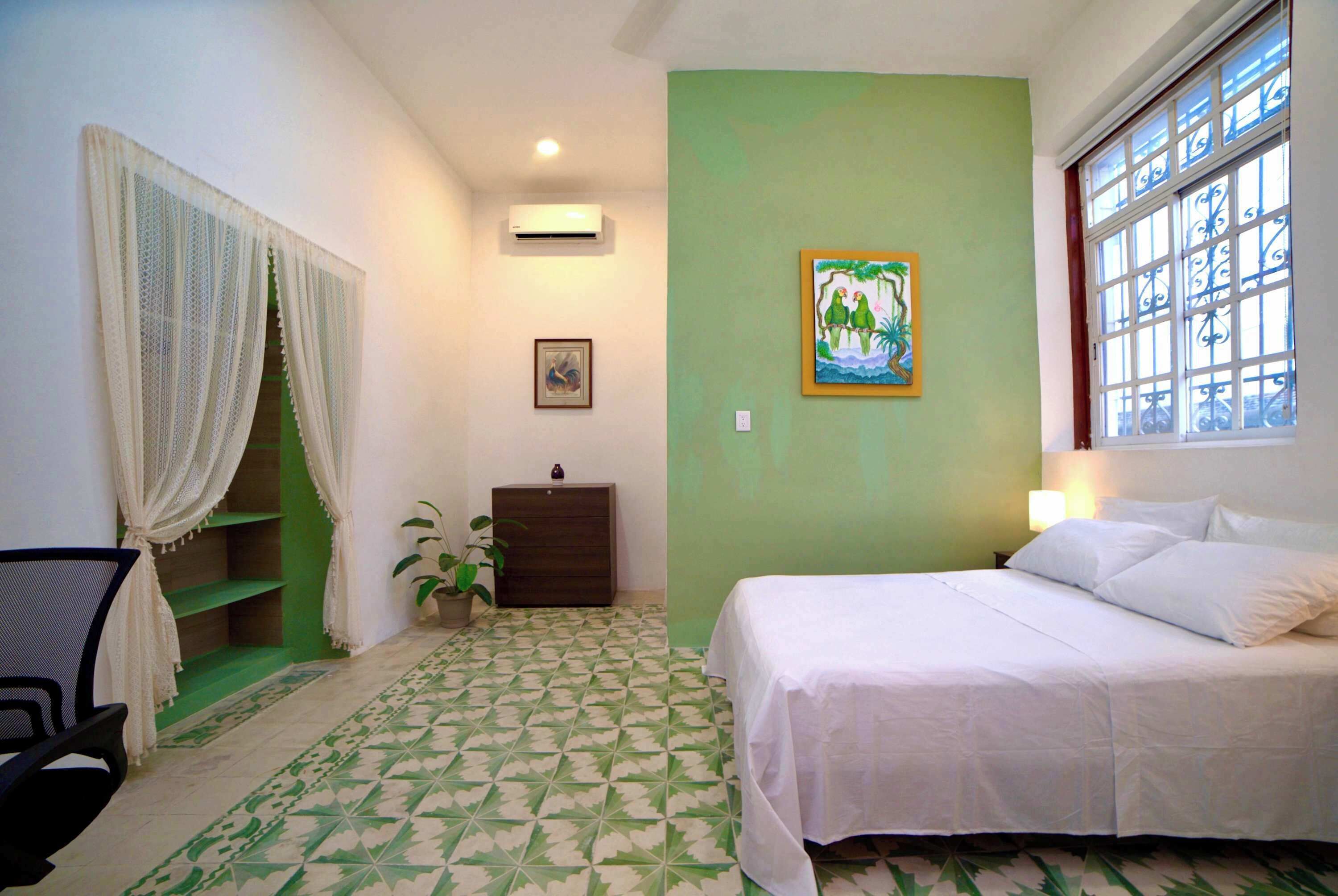 Une chambre à coucher avec un lit, une commode, une chaise, une plante en pot et un tableau accroché au mur.