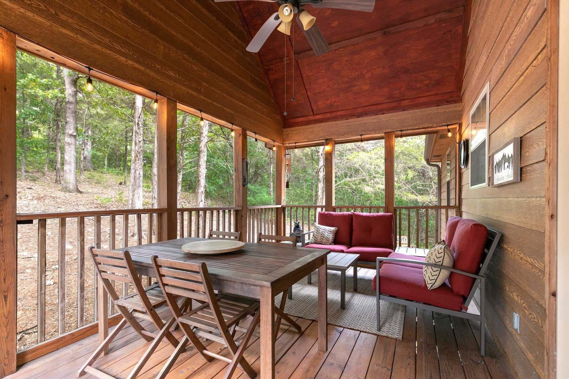 A wooden deck with a table and chairs, a red sofa, and a ceiling fan.