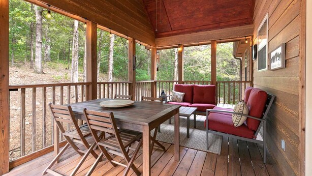 Une terrasse en bois avec une table et des chaises, un canapé rouge et un ventilateur de plafond.